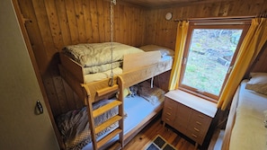 Una cama litera con escalera, un pequeño aparador y una ventana con cortinas.