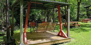 A wooden swing set with a metal roof, surrounded by grass and trees. - Hot tub, firepit, resort hiking trails, near the river, volleyball! (Sevierville)
