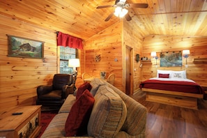 A cozy cabin interior with a wooden ceiling, a bed with a red blanket, a sofa, a chair, and a painting on the wall. - Hot tub, firepit, resort hiking trails, near the river, volleyball! (Sevierville)