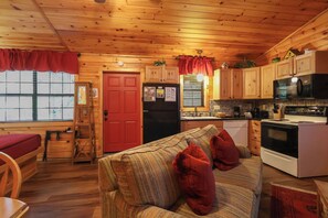 A cozy cabin interior with a wooden interior, a kitchenette, a dining area, and a living room with a sofa and pillows. - Hot tub, firepit, resort hiking trails, near the river, volleyball! (Sevierville)