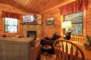 Un intérieur de chalet chaleureux avec une cheminée, des murs en bois, un téléviseur et un coin repas.
