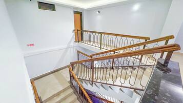 Un interior de varios niveles con una escalera de madera, paredes blancas y un cartel de 'No Smoking'.