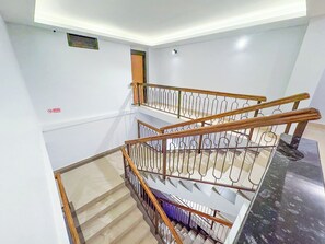 Un interior de varios niveles con una escalera de madera, paredes blancas y un cartel de 'No Smoking'.