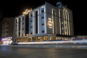 A multi-story hotel with illuminated signage, a parking lot, and a street in the foreground. - Ayas Aljouf by Suknai (Sakaka)