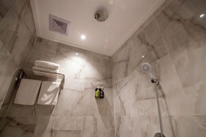 A bathroom with marble walls, a showerhead, and a towel rack with folded towels.