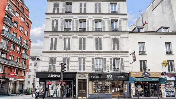 Straßenansicht mit einer Reihe von Geschäften, darunter ein Bekleidungsgeschäft, eine Apotheke und ein Imbissstand.
