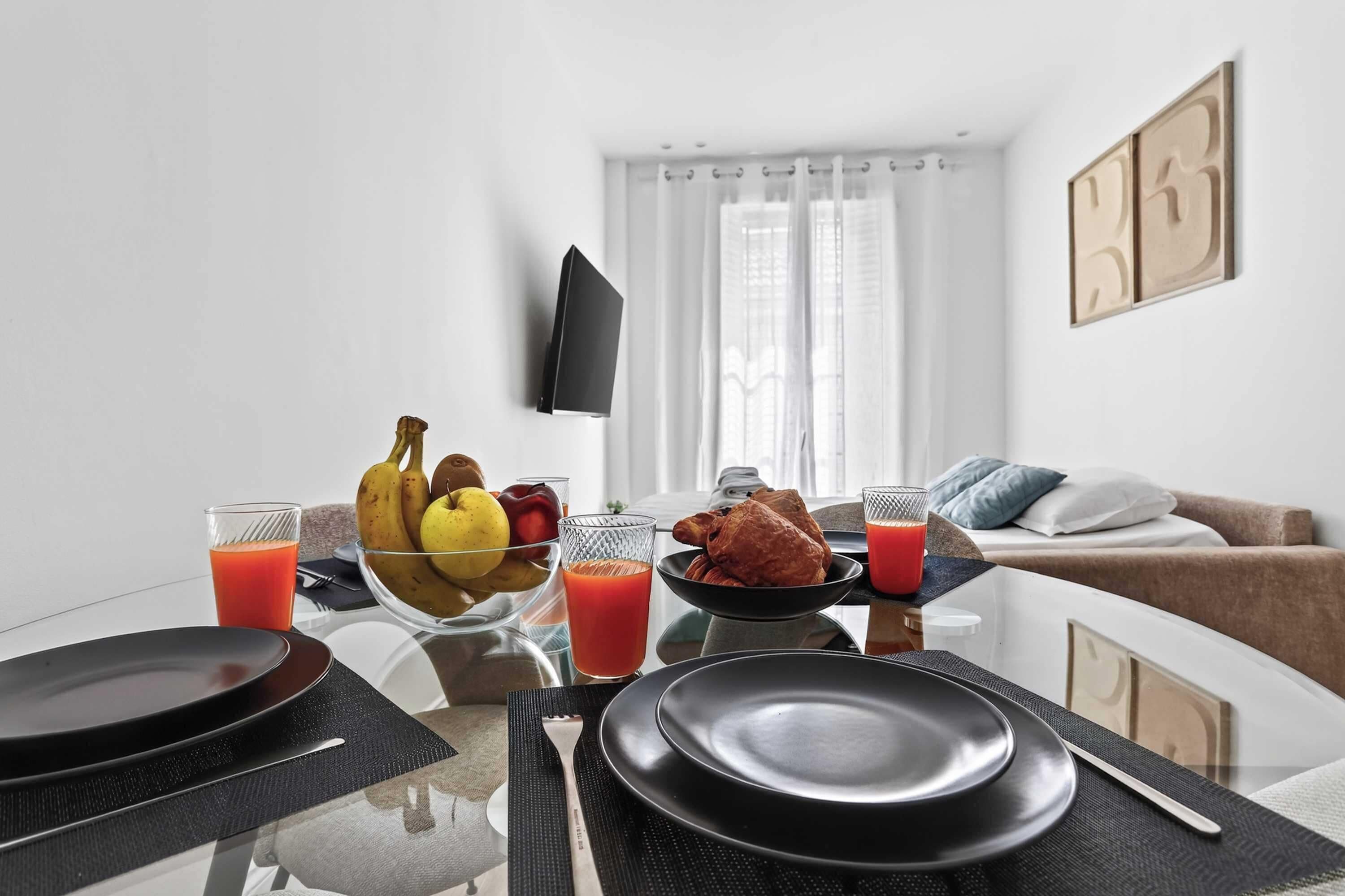 A dining table set with plates, cutlery, and a bowl of fruit and juice.