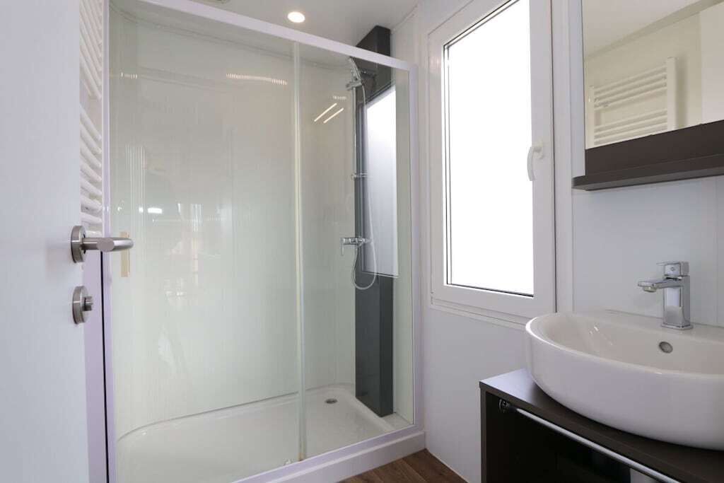 Une salle de bain moderne avec une douche à parois de verre, un lavabo blanc et un grand miroir.
