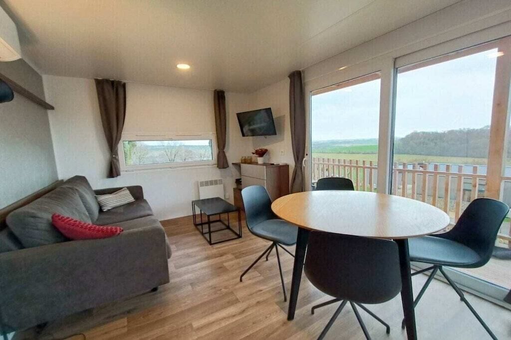 A room with a sofa, a dining table with chairs, a TV mounted on the wall, and a balcony with a view.