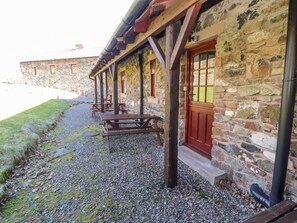 A stone building with a wooden porch and a red door. - Mellfell Cottage (Penrith)