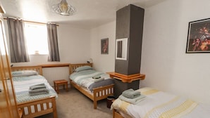 Ein Zimmer mit drei hölzernen Betten, einem Heizkörper, einem kleinen Tisch und einem fenster mit Vorhängen.