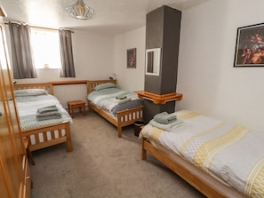 A room with three wooden beds, a radiator, a small table, and a window with curtains. - Mellfell Cottage (Penrith)