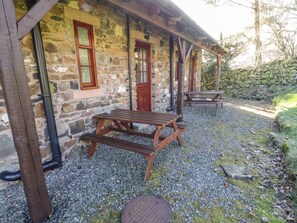 A stone building with a wooden porch, a picnic table, and a bench. - Mellfell Cottage (Penrith)