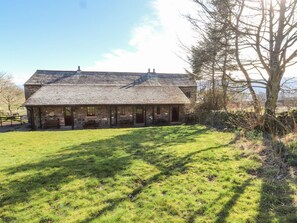 A stone building with a sloped roof, a covered porch, and a grassy yard. - Mellfell Cottage (Penrith)