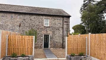 A stone building with a black door, wooden gates, and a gravel pathway leading to the entrance.