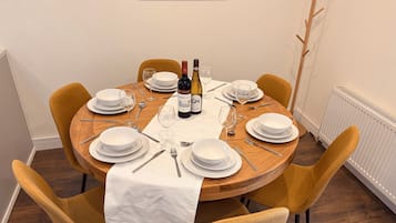 A round dining table with white plates, cutlery, and two bottles of wine.