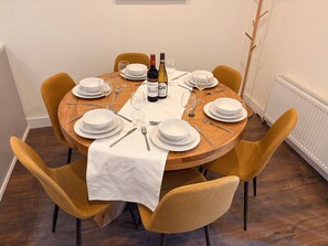 Mesa redonda para comer con platos blancos, cubiertos y dos botellas de vino.