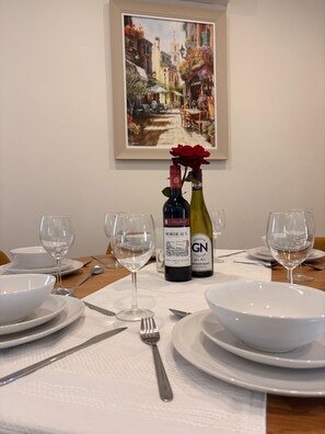 A dining table set with white plates, bowls, and wine glasses, with two wine bottles and a red rose centerpiece. - The Lodge at Sandfordscourt House - Luxury Country Stay Near Kilkenny (Sandfordscourt)