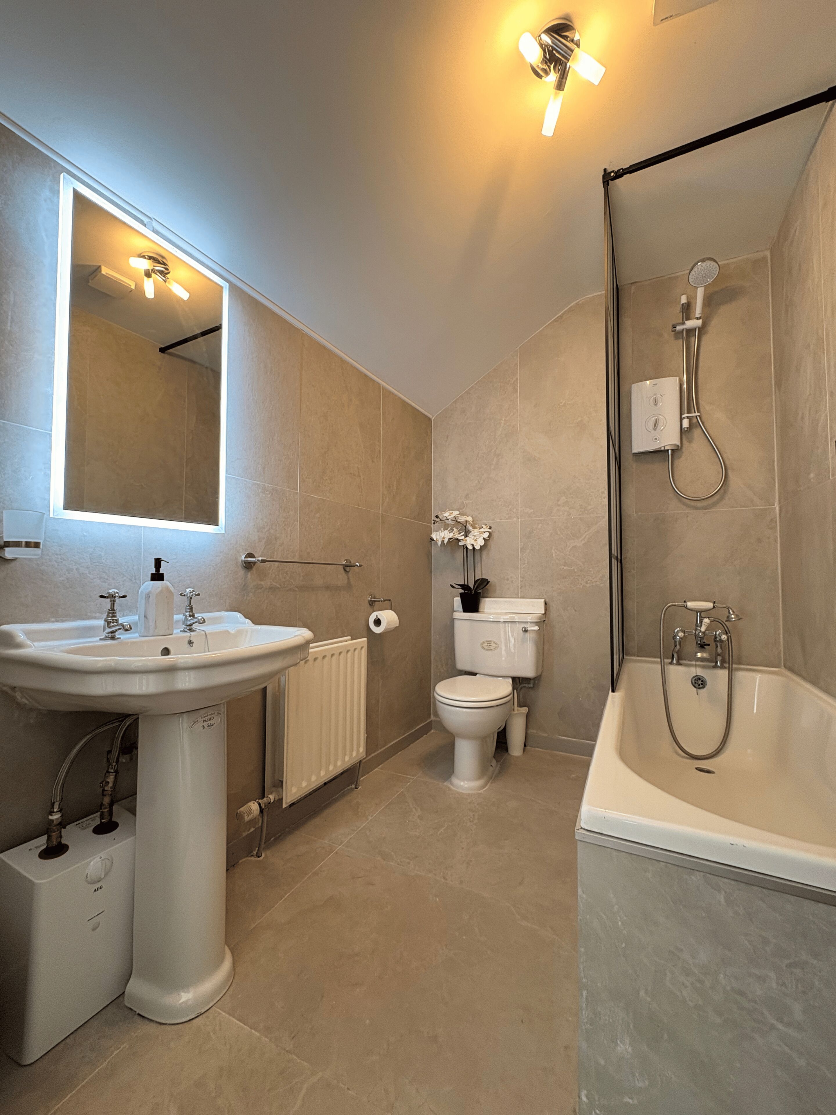 A modern bathroom with a sink, toilet, shower, and a mirror with lights.