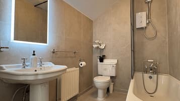 A modern bathroom with a sink, toilet, shower, and a mirror with lights.