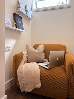 A cozy seating area with a laptop on a textured sofa, a decorative wall shelf with books and figurines, and a window with a view of the sky. - The Lodge at Sandfordscourt House - Luxury Country Stay Near Kilkenny (Sandfordscourt)