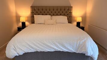A neatly made bed with a tufted headboard, two bedside lamps, and a grey upholstered bench.