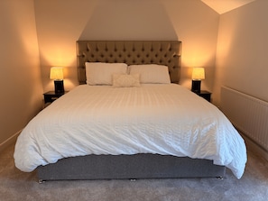 A neatly made bed with a tufted headboard, two bedside lamps, and a grey upholstered bench.