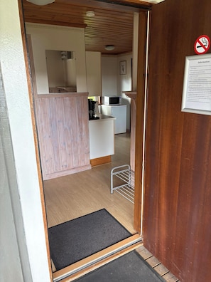 Un vano de madera da paso a una cocina con microondas, refrigerador y cafetera.
