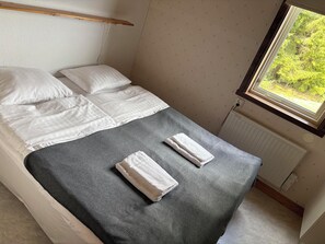 Una cama individual con sábanas blancas, una manta gris y dos toallas.