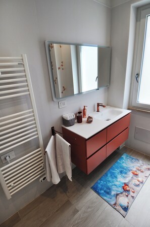 Ein modernes Badezimmer mit einem weißen Handtuchhalter, einem Spiegel über einem weißen Waschbecken mit einem Kupferarmaturen und einem Holzboden.
