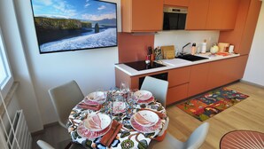 Uma cozinha moderna com forno embutido, uma mesa de jantar posta para seis pessoas com toalhas de mesa coloridas e uma grande janela com vista panorâmica.