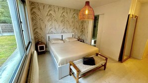 Quarto com cama, mesas de cabeceira, luminária pendente, janela e vista para o exterior.