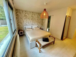 Un dormitorio con cama, mesitas de noche, lámpara colgante, ventana y vistas al exterior.