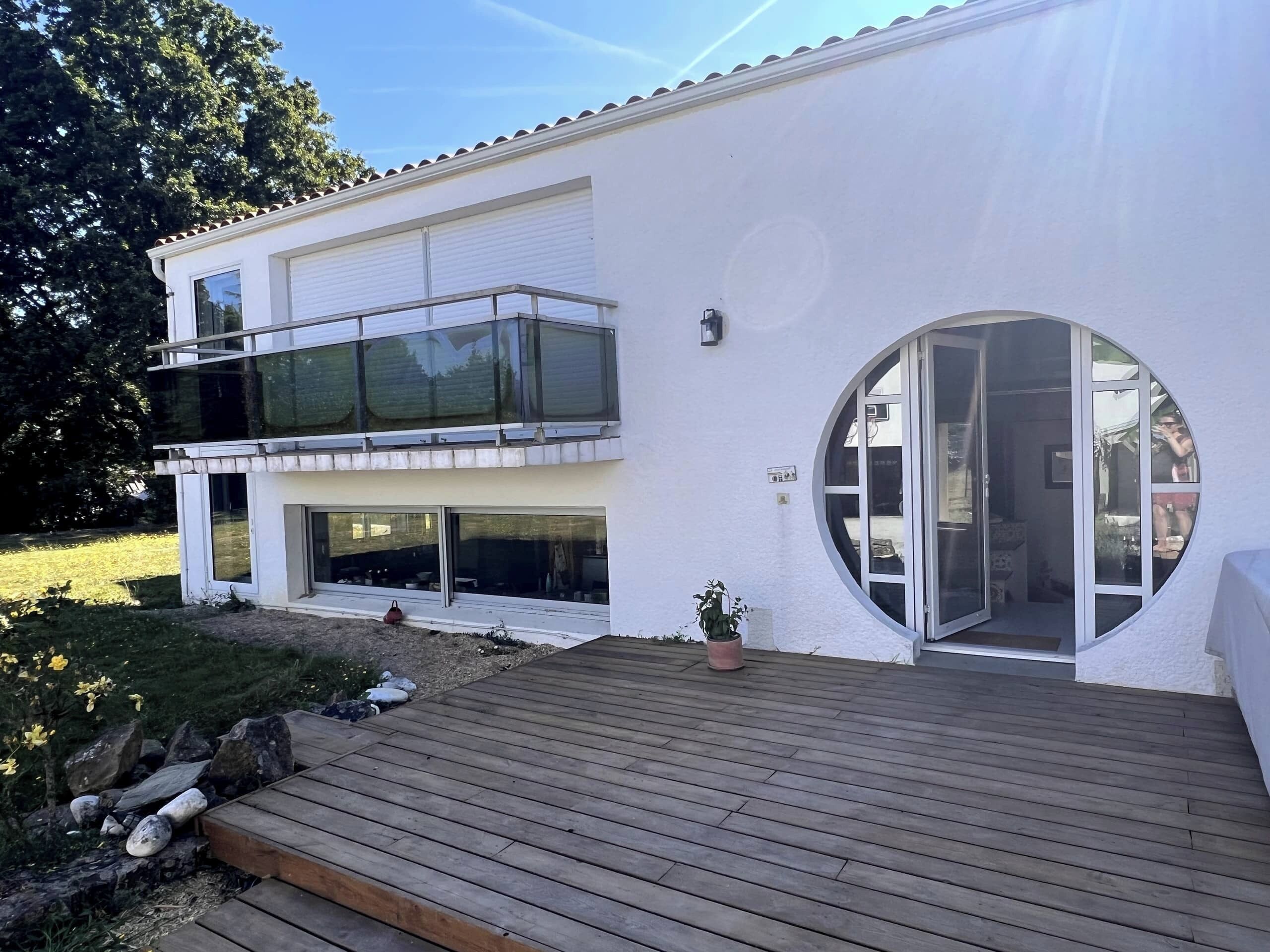 Un edificio moderno de dos pisos con un balcón, ventanas grandes y una puerta de vidrio circular.