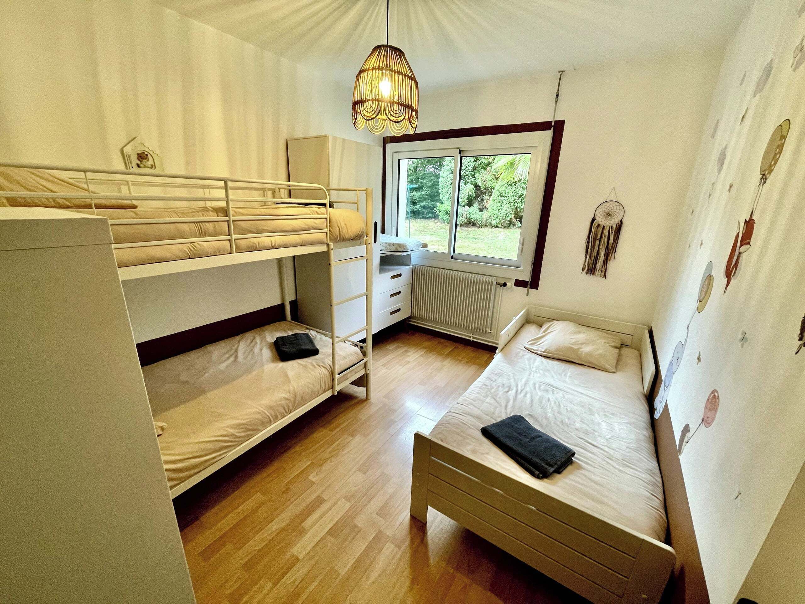 A room with bunk beds, a desk, a radiator, and a window with a view of greenery.