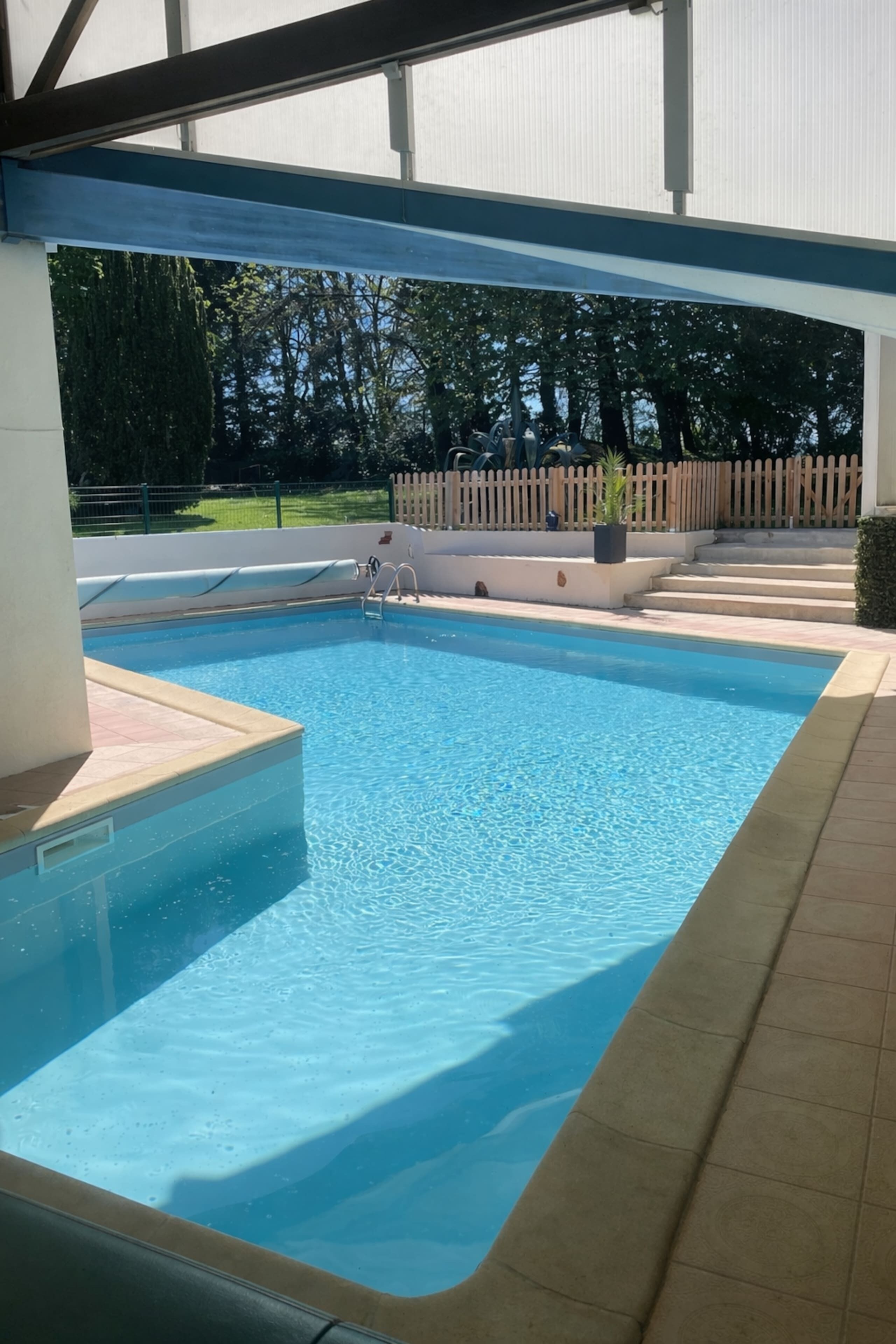 A swimming pool with a tiled deck and a wooden fence in the background.
