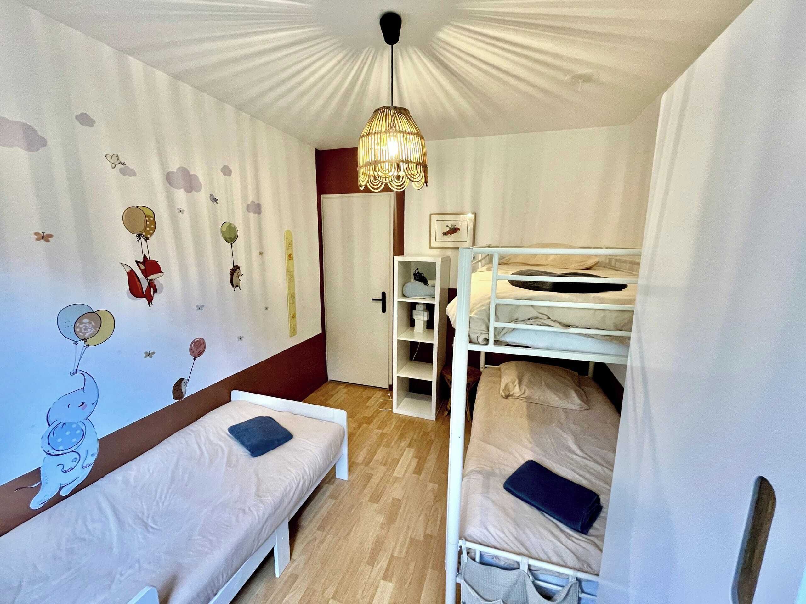 A bedroom with bunk beds, a bedside table, a wall with a children's mural, and a hanging light fixture.