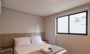 A bedroom with a bed, a nightstand, a window with a view, and a wall-mounted air conditioner. - Apt. w/ Balcony & City View Vge0303 (Blumenau)