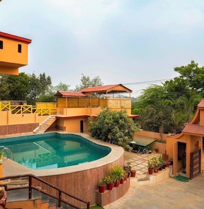 A swimming pool surrounded by a building with a red roof, a staircase, and potted plants. - Kings pride Aravali (Udaipur)