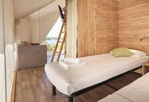 Un lit simple avec une tête de lit en bois, une petite table de chevet et une vue sur l’extérieur.