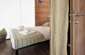 A hotel room with a bed, pillows, a bedside table, and a curtain. - Luxury Glamping Tent 4 (Gulpen)