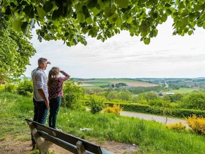 Ein Paar steht auf einer Bank und blickt auf eine ländliche Landschaft mit Feldern und einem Fluss.