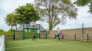A sports court with a basketball hoop, a goal, and a stone wall. - Luxury Glamping Tent 4 (Gulpen)