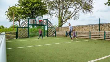 Een sportveld met een basketbalveld, een doel en een stenen muur.