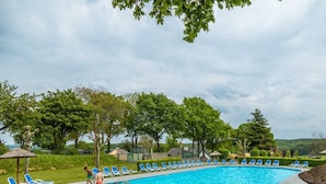 A swimming pool with blue lounge chairs, a grassy area, and trees in the background. - Luxury Glamping Tent 4 (Gulpen)