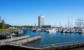A marina with multiple boats docked, a tall building in the background, and a wooden dock with railings. - Modern beachfront holiday apartment with luxury amenities on Priwall Travemünde (Lübeck)