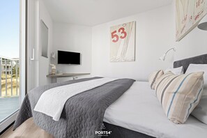 A modern bedroom with a bed, a TV, a painting, and a window. - Modern beachfront holiday apartment with luxury amenities on Priwall Travemünde (Lübeck)