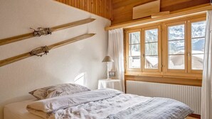 A bedroom with a wooden ceiling, a bed with white bedding, a window with curtains, and a radiator. - Chalet Rotebächli Appartement/Fewo, Bad, WC, 2 Schlafräume 4-Bettwohnung by Interhome (Lenk)