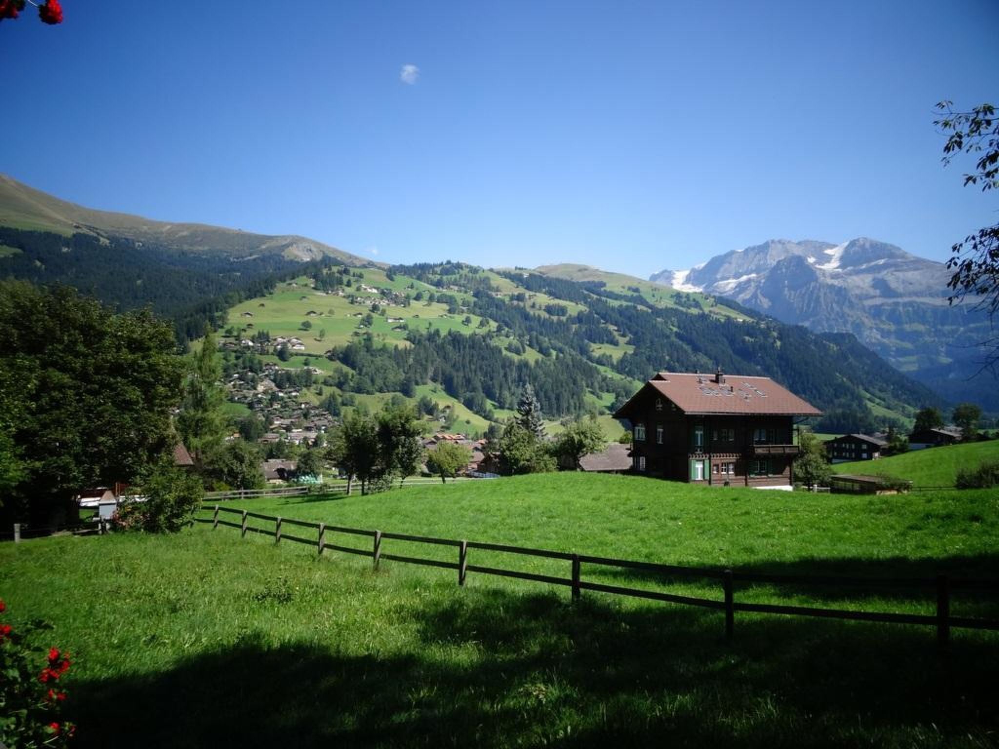 A rural landscape with a wooden house, green fields, and mountains in the background.