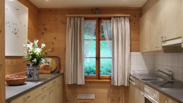 A compact kitchen with wooden cabinets, a sink, and a window with curtains. - Chalet Maru Appartement/Fewo, Dusche oder Bad, WC, 3 Schlafräume 7-Bett-Wohnung by Interhome (Lenk)